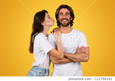 Woman kissing man on the cheek who is crossing his arms and smiling with joy 111708382