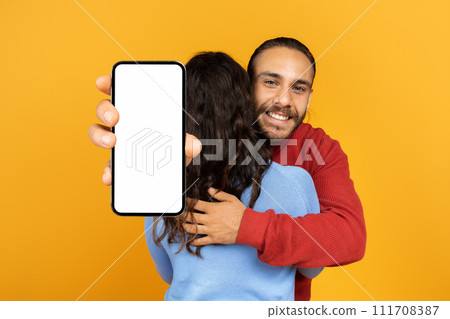 Millennial man hugging his girlfriend holding huge phone in hands 111708387