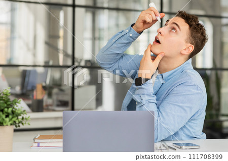 Sad tired despaired young european man manager dropping drops at dry eye, suffer from vision problems 111708399
