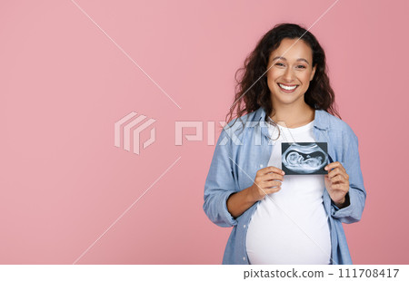 Pregnant woman holding ultrasound image of baby Pregnant woman holding ultrasound image of baby 111708417