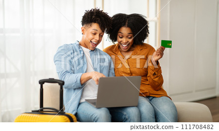 Excited young couple sitting on a couch with a laptop and a credit card 111708482