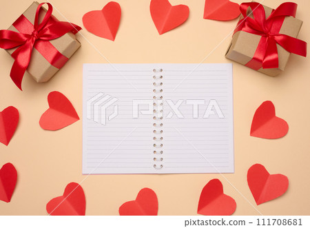 Open notebook with empty white sheets, red hearts and gift boxes on a beige background 111708681