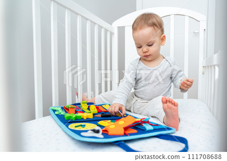 Baby playing with montessori busy book sitting in crib. Concept of smart books and modern toys Baby playing with montessori busy book sitting in crib. Concept of smart books and modern toys 111708688