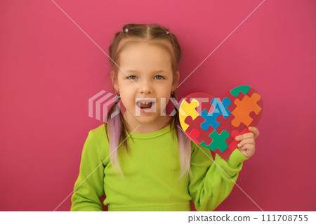 A girl talks about autism by showing a heart-shaped postcard decorated with multicolored puzzles A girl talks about autism by showing a heart-shaped postcard decorated with multicolored puzzles 111708755