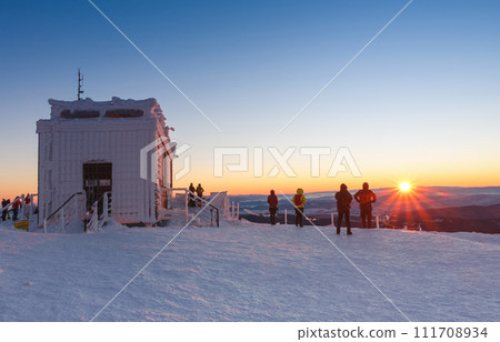 Tourists watching sunrise around wooden building of new post office with souvenirs and postcards in snezka, mountain on the border between Czech Republic and Poland, winter. Tourists watching sunrise around wooden building of new post office with souvenirs and postcards in snezka, mountain on the border between Czech Republic and Poland, winter. 111708934