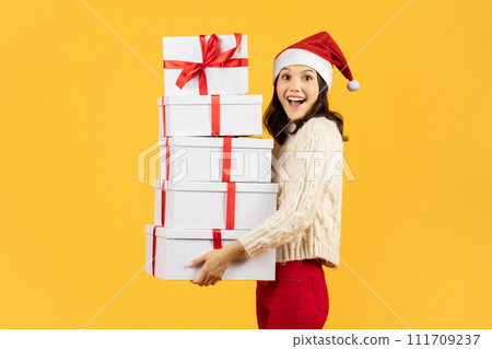 woman clutching stack of festive gifts on yellow studio background woman clutching stack of festive gifts on yellow studio background 111709237
