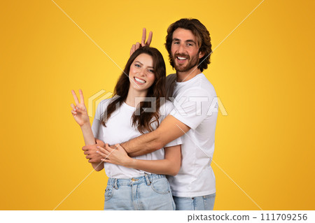 Happy couple in white shirts posing with the woman showing a peace sign and the man playfully Happy couple in white shirts posing with the woman showing a peace sign and the man playfully 111709256