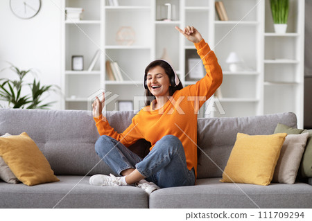 Joyful young indian woman sitting on couch, listening to music Joyful young indian woman sitting on couch, listening to music 111709294