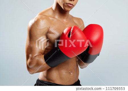 boxer wearing red boxing gloves standing shirtless over gray background 111709353