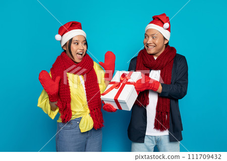 Glad millennial asian guy in hat gives box present to surprised woman Glad millennial asian guy in hat gives box present to surprised woman 111709432