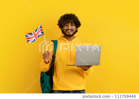 Happy young indian guy holding laptop and flag of UK 111709448