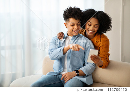 A young man in a denim shirt and a woman in a mustard top are sitting on a couch A young man in a denim shirt and a woman in a mustard top are sitting on a couch 111709450