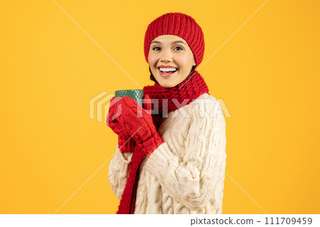 Joyful woman holds mug of coffee against yellow studio backdrop 111709459