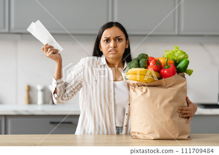 Unhappy young indian woman with grocery bag and receipt Unhappy young indian woman with grocery bag and receipt 111709484