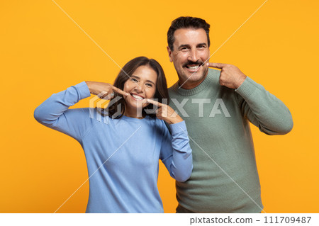 Glad senior european couple in casual point fingers at lips, make smile sign Glad senior european couple in casual point fingers at lips, make smile sign 111709487