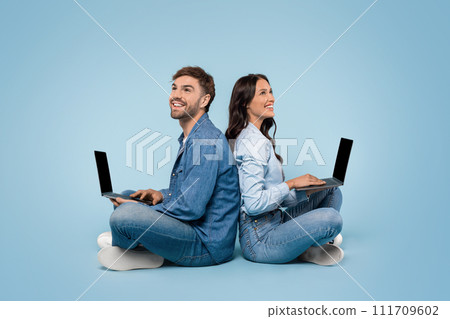 Couple sitting back-to-back with laptops, blue background Couple sitting back-to-back with laptops, blue background 111709602