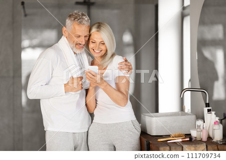Happy senior couple checking smartphone together in bathroom during their morning routine 111709734