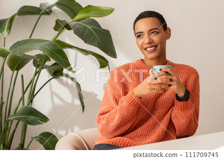 Cheerful millennial latin woman in sweater enjoy peace and spare time, drink cup of coffee Cheerful millennial latin woman in sweater enjoy peace and spare time, drink cup of coffee 111709745