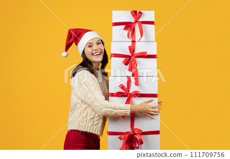 woman stands holding stack of Christmas gifts, yellow studio background woman stands holding stack of Christmas gifts, yellow studio background 111709756