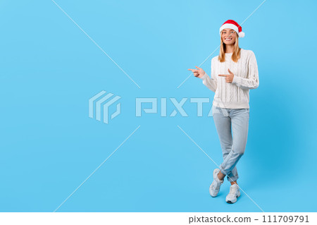 Cheerful woman with Santa hat pointing away at free space Cheerful woman with Santa hat pointing away at free space 111709791