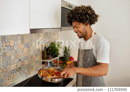 African man stirs vegetarian stew cooking vegetable meal in kitchen 111709990