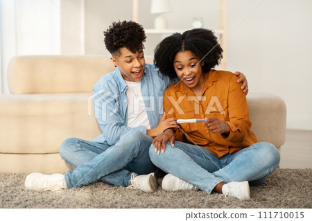 An overjoyed young couple sits on the floor with a positive pregnancy test 111710015