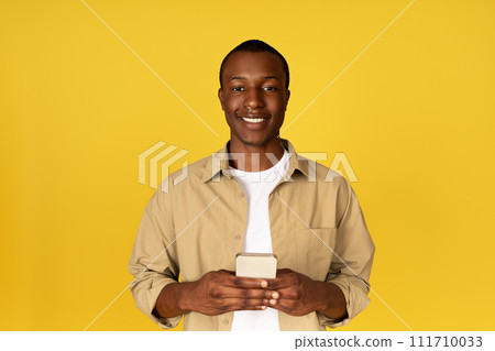 Cheerful millennial black guy in casual chatting on phone, isolated on yellow studio background Cheerful millennial black guy in casual chatting on phone, isolated on yellow studio background 111710033