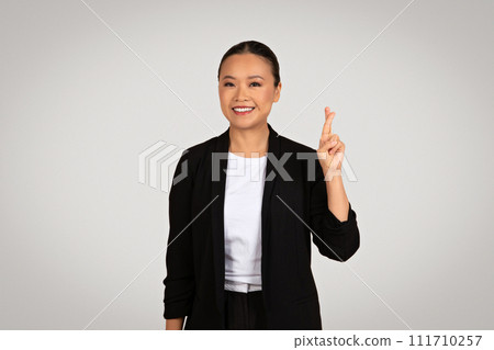 A poised Asian businesswoman in a smart black jacket displays a victory sign with a joyful A poised Asian businesswoman in a smart black jacket displays a victory sign with a joyful 111710257