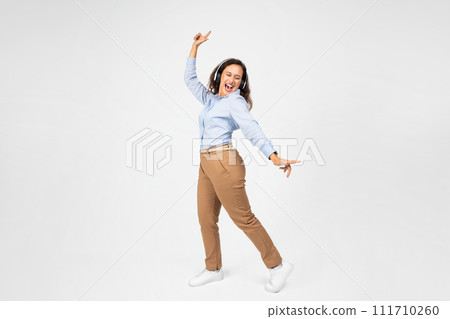 A lively young woman with curly hair, dressed in a blue shirt and brown pants 111710260