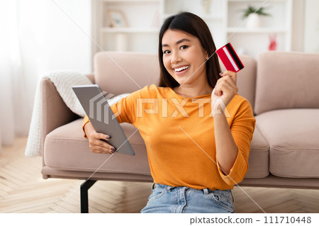 Positive young asian woman using credit card and digital tablet 111710448