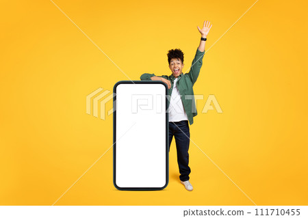 Joyful young black guy stand by huge phone, gesturing Joyful young black guy stand by huge phone, gesturing 111710455