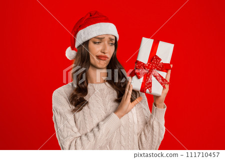 woman looks disappointed holding gift box on red studio background 111710457
