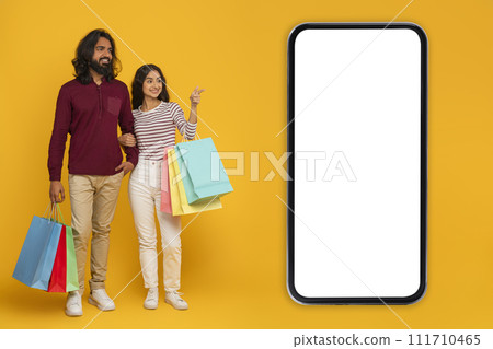 Happy young indian couple shopping together on yellow, mobile app Happy young indian couple shopping together on yellow, mobile app 111710465