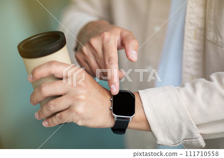 Man with cup of coffee checking time on smart watch Man with cup of coffee checking time on smart watch 111710558