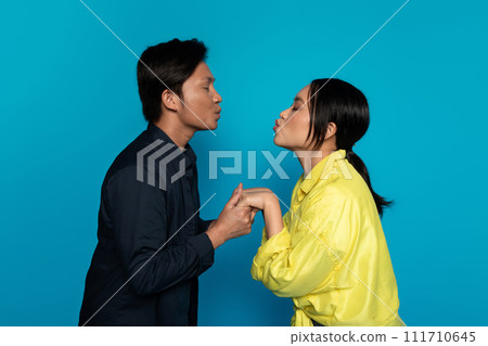 Happy young japanese guy and woman in casual kisses, isolated on blue studio background 111710645