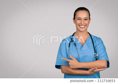Positive nurse lady in blue workwear advertising space for advertisement, pointing finger aside, medical offer text Positive nurse lady in blue workwear advertising space for advertisement, pointing finger aside, medical offer text 111710653