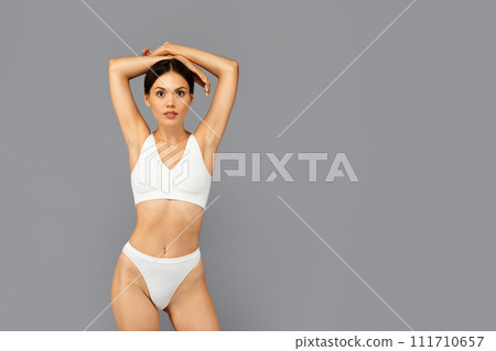 Calm asian young woman in white underwear confidently poses against grey background Calm asian young woman in white underwear confidently poses against grey background 111710657