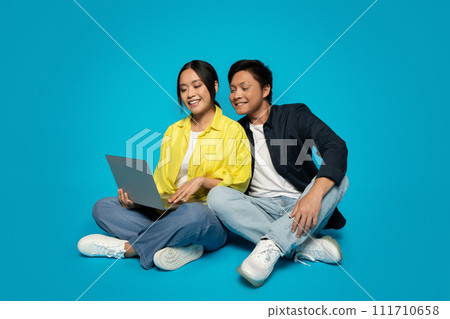 Two cheerful young adults, a woman in a yellow jacket using a laptop and a man 111710658
