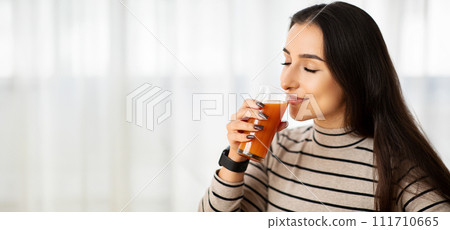 Savoring the moment, a young woman in a striped turtleneck gently enjoys her carrot juice Savoring the moment, a young woman in a striped turtleneck gently enjoys her carrot juice 111710665