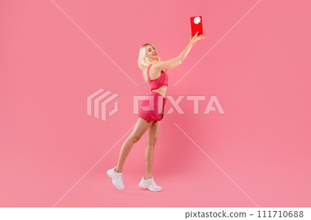 Ecstatic young woman tossing gift in the air, pink background Ecstatic young woman tossing gift in the air, pink background 111710688