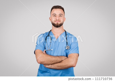 Confident male doctor in blue coat, arms folded, grey background Confident male doctor in blue coat, arms folded, grey background 111710736