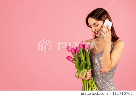 A radiant young woman in a glittery dress enjoys a cheerful conversation on her smartphone 111710765
