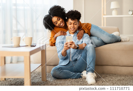 A relaxed and happy young couple lounges on the floor, leaning against a sofa 111710771