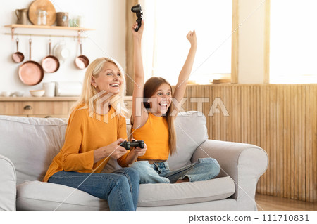 Happy modern grandmother and girl teenager granddaughter playing video games 111710831