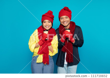 Smiling young asian family couple in hats and scarves warming up with cups of hot drink takeaway 111710832