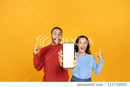 Beautiful millennial couple holding huge phone in hands Beautiful millennial couple holding huge phone in hands 111710845
