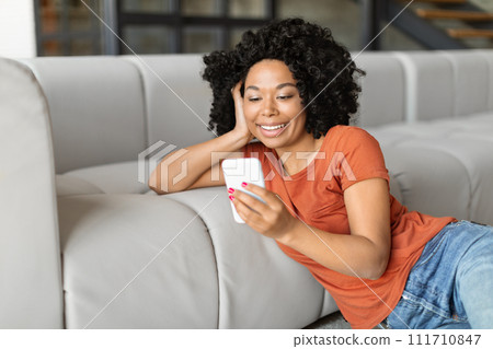 Smiling Black Woman Watching Videos On Smartphone At Home Smiling Black Woman Watching Videos On Smartphone At Home 111710847