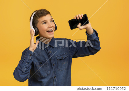 Cheerful teen boy in wireless headphones listening music on smartphone and singing 111710952