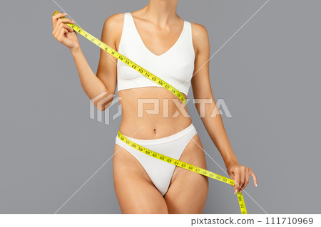 Young european lady in white sportswear use yellow measuring tape around body to highlight fitness progress Young european lady in white sportswear use yellow measuring tape around body to highlight fitness progress 111710969