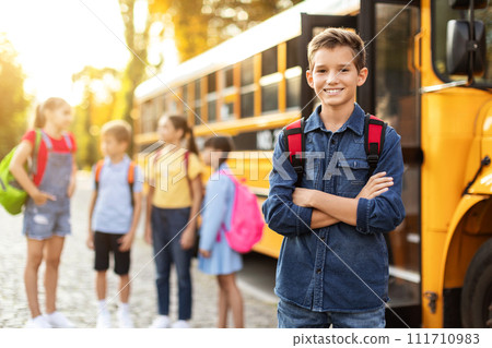 Smiling Preteen Boy Standing With Folded Arms Near Yellow School Bus 111710983